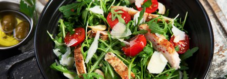 Téléchargez les photos : Chicken breast and fresh vegetable salad of lettuce, arugula, spinach, parmesan and tomatoes in dark plate. Healthy mediterranean dish. Keto Diet eating. Top view, panorama, banner - en image libre de droit