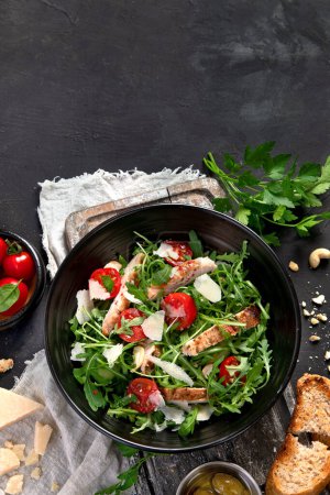 Téléchargez les photos : Chicken breast and fresh vegetable salad of lettuce, arugula, spinach, parmesan and tomatoes in dark plate. Healthy mediterranean dish. Keto Diet eating. Top view, copy space - en image libre de droit