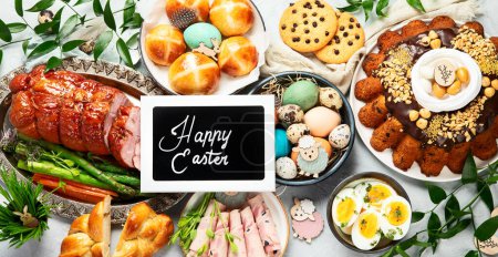 Téléchargez les photos : Classic Easter ham dinner. Top view table scene on a white background. Ham, eggs, hot cross buns, carrot, cake and vegetables. - en image libre de droit