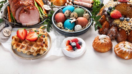 Téléchargez les photos : Traditional Easter dinner or  brunch with ham, colored eggs, hot cross buns, cake and vegetables. Easter meal dishes with holday decorations. - en image libre de droit