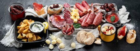 Photo for Typical spanish tapas with jamon slices, chorizo, salami,  olives,  potatoes snack Patatas bravas, seafoods on dark table. Traditional spanish food. Top view, panorama, banner - Royalty Free Image