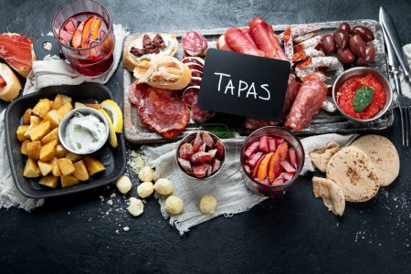 Photo for Typical spanish tapas with jamon slices, chorizo, salami,  olives,  potatoes snack Patatas bravas, seafoods on dark table. Traditional spanish food. Top view - Royalty Free Image