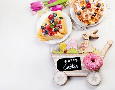 Téléchargez les photos : Easter sweet dessert table. Pancakes, crepes, waffles and donuts  with fresh berries, nuts and topping.   Easter traditional natural colorful eggs. Top view, copy space - en image libre de droit