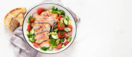 Foto de Grilled chicken breast, fillet and fresh vegetable salad of lettuce, arugula, spinach, cucumber and tomato on a white background. Healthy lunch menu. Diet food. Top view. Panorama with copy space. - Imagen libre de derechos