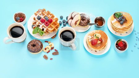 Foto de Summer or spring breakfast with Cup of hot cappuccino coffee,  pancakes, waffles coffee, tulips  flowers, craft envelope on blue background.  Top view, flat lay, copy space - Imagen libre de derechos