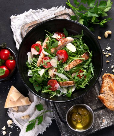 Photo for Chicken breast and fresh vegetable salad of lettuce, arugula, spinach, parmesan and tomatoes in dark plate. Healthy mediterranean dish. Keto Diet eating. Top view - Royalty Free Image