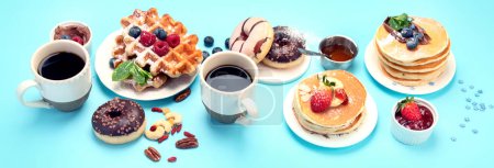 Téléchargez les photos : Summer or spring breakfast with Cup of hot cappuccino coffee,  pancakes, waffles coffee, tulips  flowers, craft envelope on blue background.  TPanorama, banner, flat lay, - en image libre de droit