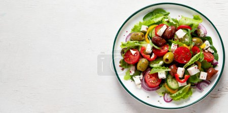 Téléchargez les photos : Greek salad of fresh cucumber, tomato, sweet pepper, lettuce, red onion, feta cheese and olives with olive oil on a white background. Healthy food, top view.  Panorama with copy space. - en image libre de droit