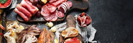 Photo for Typical spanish tapas with jamon slices, chorizo, salami,  olives,  potatoes snack Patatas bravas, seafoods on dark table. Traditional spanish food. Top view. copy space, panorama, banner - Royalty Free Image