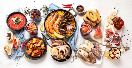 Photo for Typical spanish tapas concept. Concept include jamon, chorizo sausage, brushettas, bowl with olives, shrimp, pan with paella, cheese, sangria, churros on a white background. Top view. - Royalty Free Image