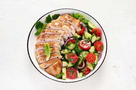 Foto de Grilled chicken breast, fillet and fresh vegetable salad of lettuce, arugula, spinach, cucumber and tomato on a white background. Healthy lunch menu. Diet food. Top view. - Imagen libre de derechos
