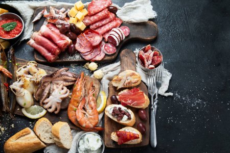 Photo for Typical spanish tapas with jamon slices, chorizo, salami,  olives,  potatoes snack Patatas bravas, seafoods on dark table. Traditional spanish food. Top view. copy space - Royalty Free Image