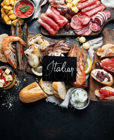 Photo for Typical italian tapas with jamon slices, chorizo, salami,  olives,  potatoes snack Patatas bravas, seafoods on dark table. Traditional italian food. Top view. - Royalty Free Image