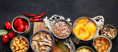 Photo for Various canned vegetables, meat, fish and fruits in tin cans. On a dark background. Top view. Panorama with copy space. - Royalty Free Image