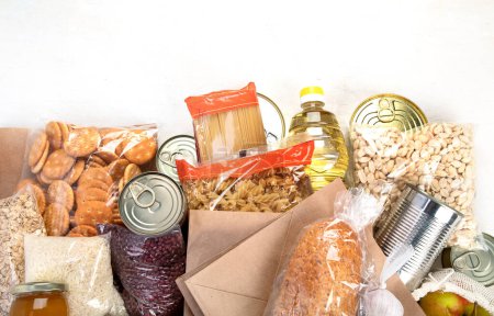 Téléchargez les photos : Food donations with pasta, rice, oil, peanut butter, canned food, jam and other  on light background, top view with copy space. Food donations or delivery concept. - en image libre de droit