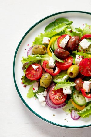 Photo for Greek salad of fresh cucumber, tomato, sweet pepper, lettuce, red onion, feta cheese and olives with olive oil on a white background. Healthy food, top view. - Royalty Free Image