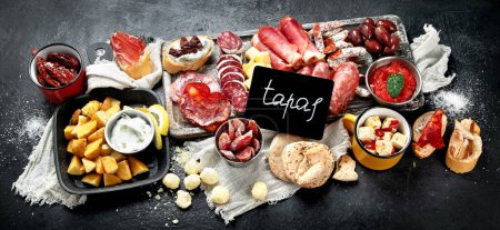 Photo for Typical spanish tapas with jamon slices, chorizo, salami,  olives,  potatoes snack Patatas bravas, seafoods on dark table. Traditional spanish food. Top view. copy space - Royalty Free Image