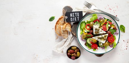 Foto de Greek salad of fresh cucumber, tomato, sweet pepper, lettuce, red onion, feta cheese and olives with olive oil on a white background. Healthy food, top view. Panorama with copy space. - Imagen libre de derechos