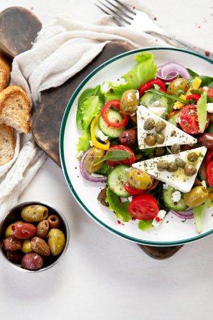 Foto de Greek salad of fresh cucumber, tomato, sweet pepper, lettuce, red onion, feta cheese and olives with olive oil on a white background. Healthy food, top view. - Imagen libre de derechos
