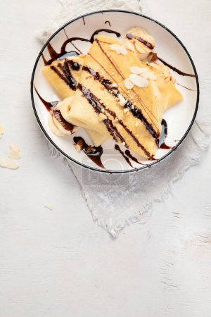 Photo for Crepe with banana, chopped almonds and chocolate sauce on white plate, table top view on a white background. Delicious french style crepes. - Royalty Free Image