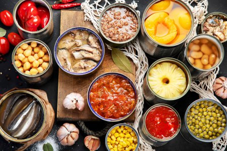 Photo for Various canned vegetables, meat, fish and fruits in tin cans. On a dark background. Top view. - Royalty Free Image