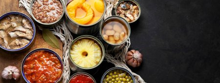 Photo for Various canned vegetables, meat, fish and fruits in tin cans. On a dark background. Top view. Panorama with copy space. - Royalty Free Image