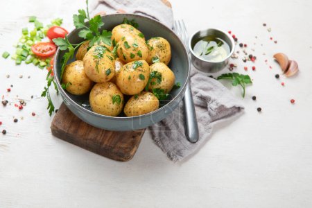 Téléchargez les photos : Les jeunes pommes de terre bouillies sur l'assiette avec du persil et de l'oignon sur la planche. Fond blanc. Vue du dessus. - en image libre de droit