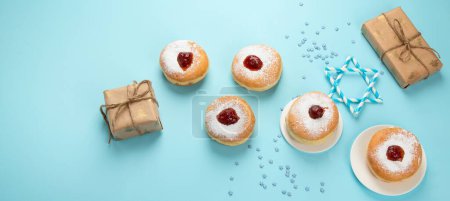 Photo for Hanukkah sweet doughnuts sufganiyot (traditional donuts) with fruit jelly jam and white candles on blue paper background. Jewish holiday Hanukkah concept. Panorama with copy space. - Royalty Free Image
