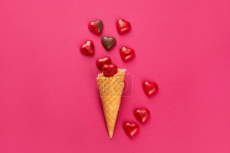 Foto de Dulces de chocolate envueltos y sin envolver en forma de corazón en papel de aluminio rojo sobre fondo rosa. Concepto de amor, vista superior - Imagen libre de derechos