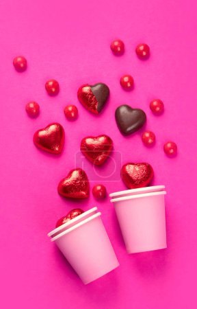 Téléchargez les photos : Bonbons au chocolat en forme de coeur enveloppés et déballés en papier d'aluminium rouge sur fond rose. Concept d'amour, vue de dessus - en image libre de droit