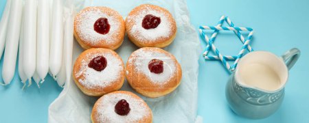 Photo for Hanukkah sweet doughnuts sufganiyot (traditional donuts) with fruit jelly jam and white candles on blue paper background. Jewish holiday Hanukkah concept. Panorama. - Royalty Free Image