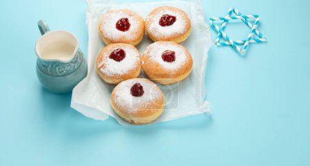 Photo for Hanukkah sweet doughnuts sufganiyot (traditional donuts) with fruit jelly jam and white candles on blue paper background. Jewish holiday Hanukkah concept. Copy space. - Royalty Free Image