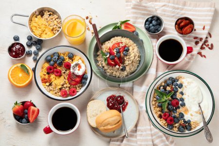 Photo for Breakfast food table. Healthy breakfast or brunch set, meal variety with granola, porridge, cornflakes, fresh berries, fruits and various of topping on a white background. Top view. - Royalty Free Image