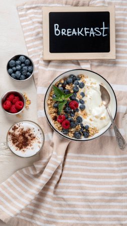 Téléchargez les photos : Granola avec yaourt et baies pour un petit déjeuner sain. Bol de yaourt grec avec granola, bleuets et framboises sur fond blanc, vue sur le dessus. - en image libre de droit
