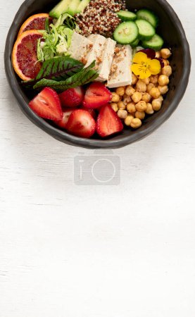 Photo for Healthy vegan lunch bowl. Avocado, quinoa, cucumber, red orange, chickpea, cheese, salad and strawberries on a white background. Top view. Copy space. - Royalty Free Image