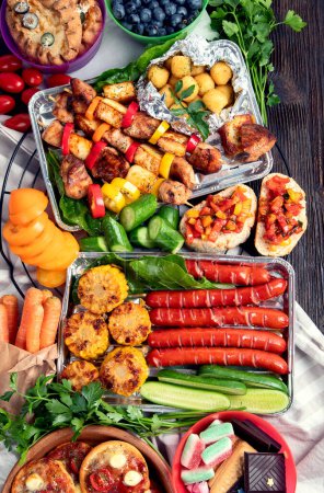 Téléchargez les photos : Divers repas grillés - viandes grillées, légumes, fruits, salade et pommes de terre sur un fond de bois sombre. Vue du dessus. - en image libre de droit