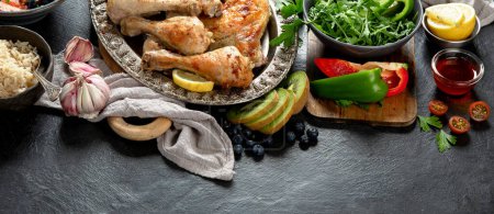 Photo for Chicken legs with rice, vegetable salads and sauce on a dark background. Healthy dinner concept. Top view. Copy space. - Royalty Free Image