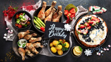 Foto de Cena con pollo, verduras, tarta, ensalada y frutas sobre un fondo oscuro. Concepto de comida de verano. Vista superior. - Imagen libre de derechos