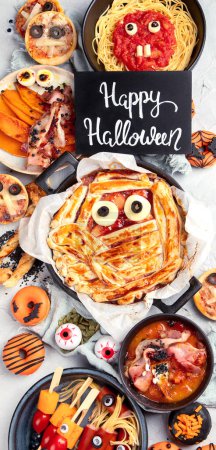Téléchargez les photos : Fun Halloween dîner scène de table de fête sur un fond gris. Vue de dessus. Pizza, tarte, spaghettis et collations - en image libre de droit