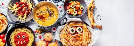 Photo for Fun Halloween dinner party table scene on a grey background. Top view. Pizza, pie, spaghetti and snacks. Panorama with copy space - Royalty Free Image
