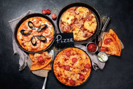 Foto de Surtido de varios tipos de pizza italiana sobre un fondo negro, vista superior. - Imagen libre de derechos
