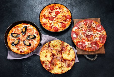 Foto de Surtido de varios tipos de pizza italiana sobre un fondo negro, vista superior. - Imagen libre de derechos