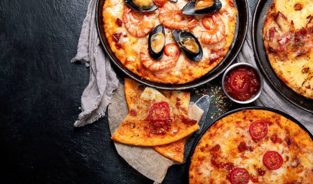 Téléchargez les photos : Assortiment de différents types de pizza italienne sur fond noir, vue de dessus. Panorama avec espace de copie. - en image libre de droit