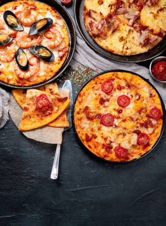 Foto de Surtido de varios tipos de pizza italiana sobre un fondo negro, vista superior. Copiar espacio. - Imagen libre de derechos
