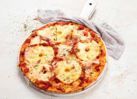 Foto de Pizza tropical hawaiana con rodajas de piña y jamón sobre una tabla sobre fondo blanco, vista superior - Imagen libre de derechos
