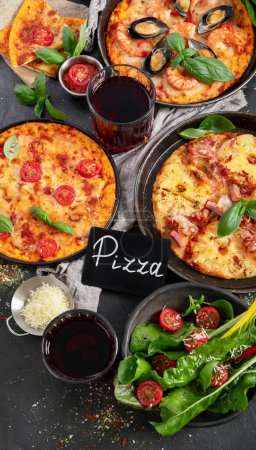Téléchargez les photos : Dîner pizza. Table avec différents types de pizza italienne, salade et vin rouge sur fond noir, vue sur le dessus. - en image libre de droit