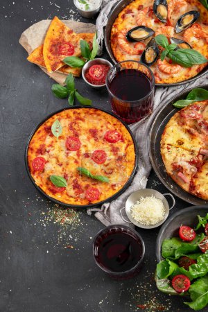 Téléchargez les photos : Dîner pizza. Table avec différents types de pizza italienne, salade et vin rouge sur fond noir, vue sur le dessus. - en image libre de droit