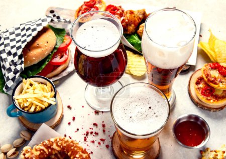 Photo for Fast food dish. Juicy burger, chicken wings, snacks, sauces and glasses of cold beer on light background. Top view. - Royalty Free Image
