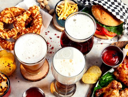Photo for Fast food dish. Juicy burger, chicken wings, snacks, sauces and glasses of cold beer on light background. Top view. - Royalty Free Image