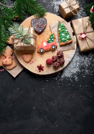 Téléchargez les photos : Biscuits de Noël, chocolat de Noël traditionnel Pains d'épice avec décoration de vacances, cadeaux, branche d'arbre de Noël sur fond sombre, vue sur le dessus. Espace de copie. - en image libre de droit